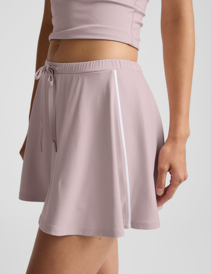Side view of the pink Sport Active Drawcord Mini Skirt with white side piping and an elastic waist with a tied drawcord.