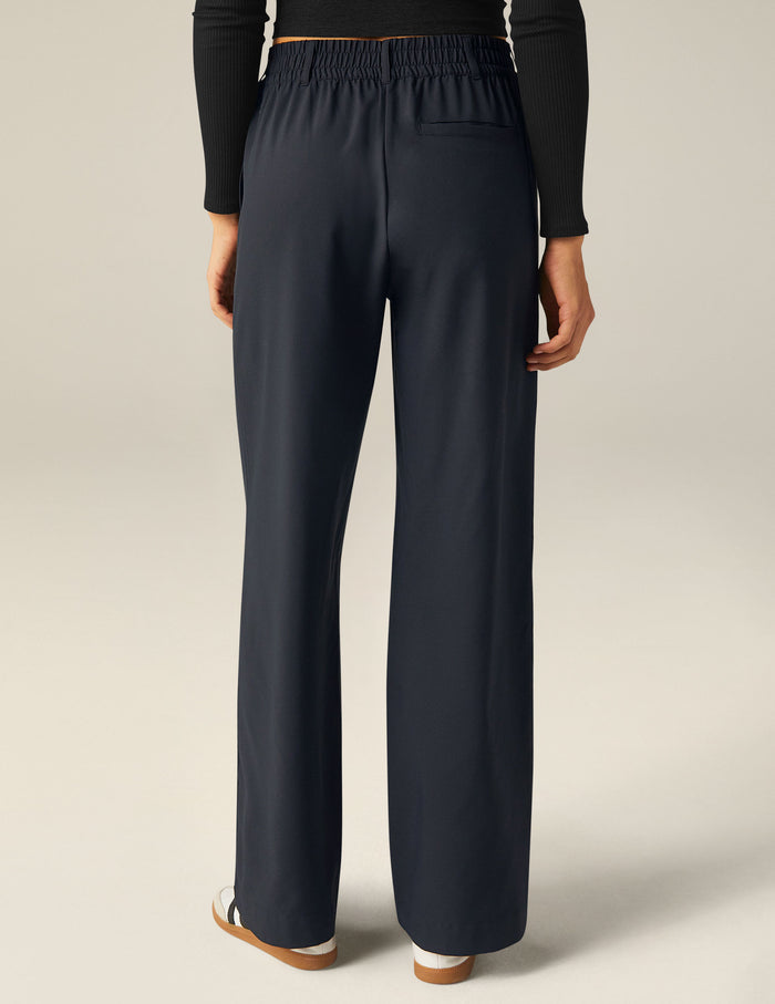 Woman wearing Black Status™ Wide Leg Trousers from the rear view, paired with a black top and white sneakers.
