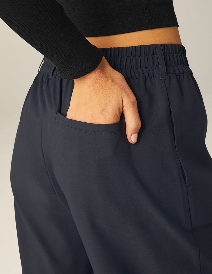 Woman wearing Black Status Wide Leg Trousers with hand in back welt pocket, paired with a black long-sleeve ribbed top.