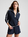 Woman wearing a blue quarter zip jacket and blue shorts against a plain background.