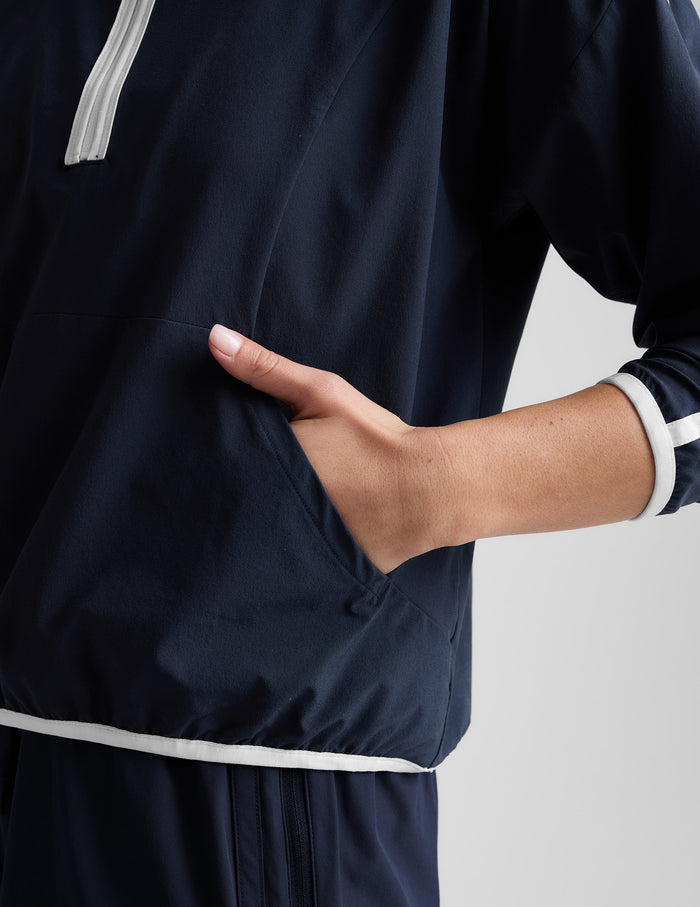 Woman wearing a blue quarter zip jacket and blue shorts against a plain background.