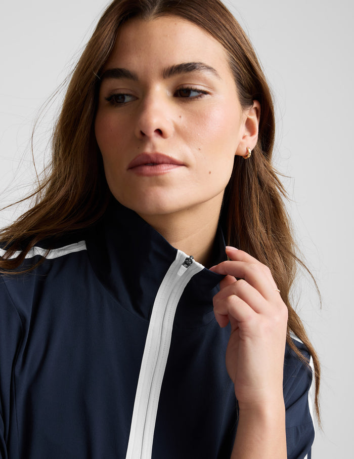 Woman wearing a blue quarter zip jacket and blue shorts against a plain background.