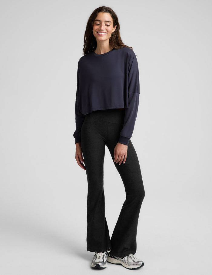 A woman modeling a dark navy blue long-sleeve crop top, paired with black leggings, against a solid light gray background.