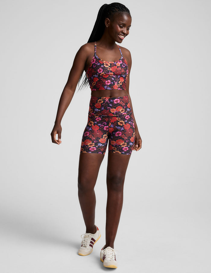 A model wears the Summer Bouquet SoftMark Keep Pace Biker Short featuring a dark floral print and high waistband.
