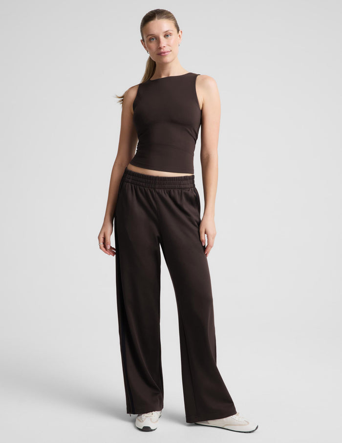 A woman modeling a dark brown sleeveless tank top and matching wide-leg pants against a light gray studio background.