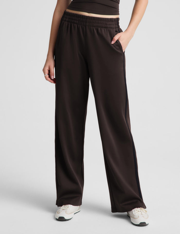 A woman modeling a dark brown sleeveless tank top and matching wide-leg pants against a light gray studio background.