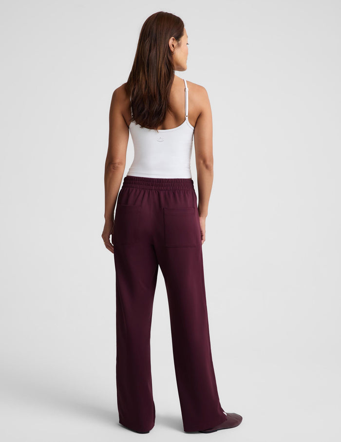 A woman shown from the back wearing a white camisole top and dark burgundy wide-leg pants against a light gray studio background.
