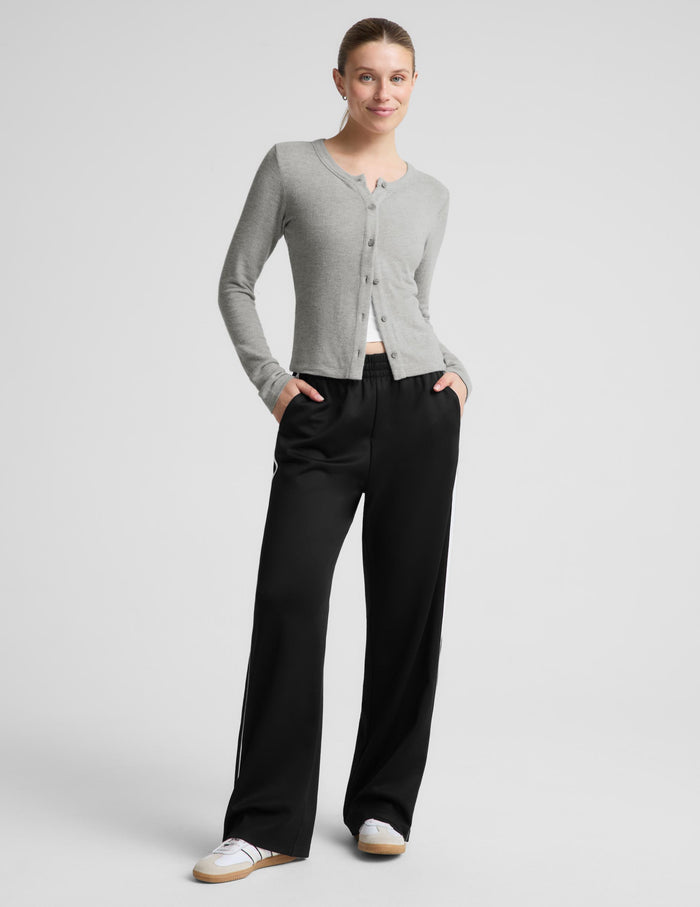 A woman modeling a gray cardigan and black wide-leg track pants against a light gray studio background.