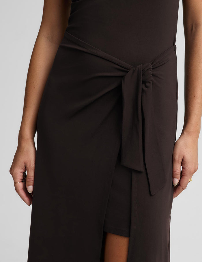 Close-up of a dark brown wrap-style midi dress worn by a model, featuring a knotted waist tie and a front slit.