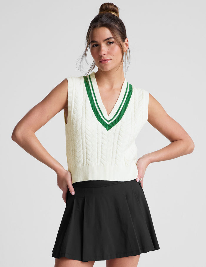white relaxed fit cable knit vest with a neckline with contrast color stripe​, rib hemband, neckline and armhole​s.