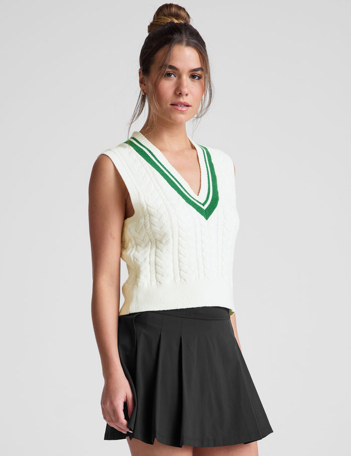 white relaxed fit cable knit vest with a neckline with contrast color stripe​, rib hemband, neckline and armhole​s.