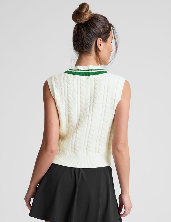 white relaxed fit cable knit vest with a neckline with contrast color stripe​, rib hemband, neckline and armhole​s.