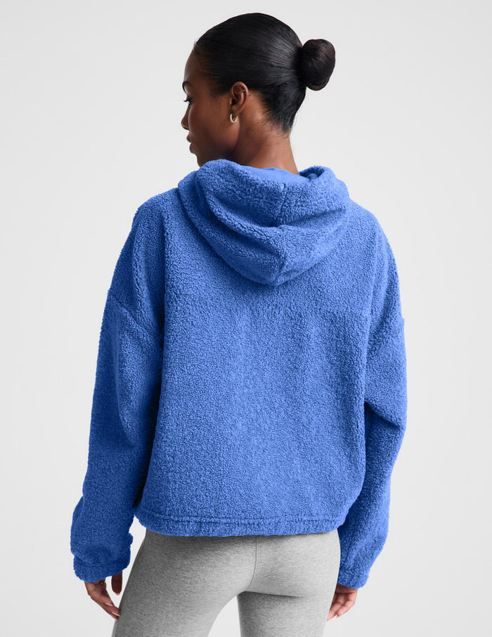 A woman wearing a textured blue fleece quarter-zip pullover sweater and gray leggings, posing against a light gray studio background.