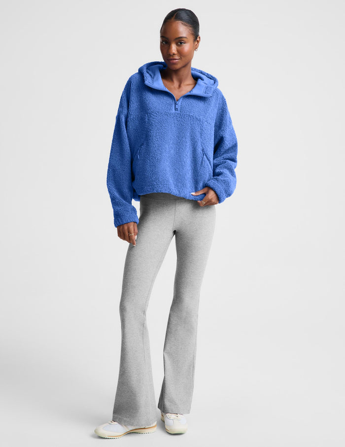 A woman wearing a textured blue fleece quarter-zip pullover sweater and gray leggings, posing against a light gray studio background.