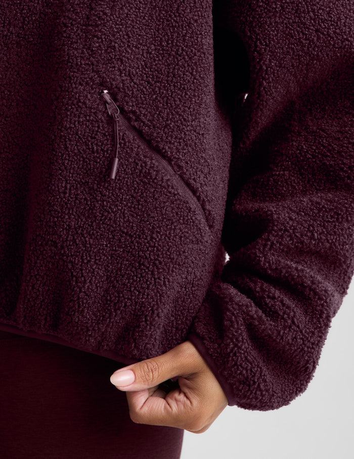 A woman wearing a dark burgundy boucle zip-up jacket and matching leggings, posing against a light gray studio background.