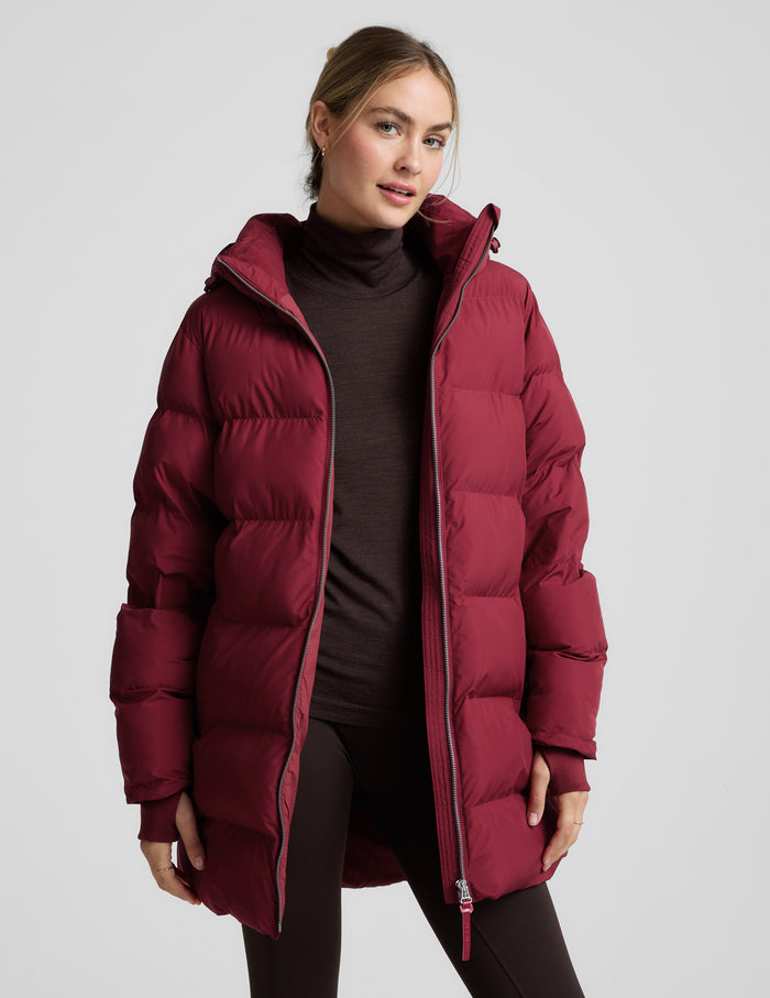 Woman wearing a red puffer coat on a light gray background.