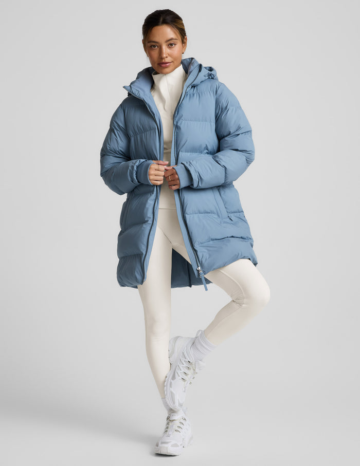 Woman wearing a blue puffer coat on a light gray background.