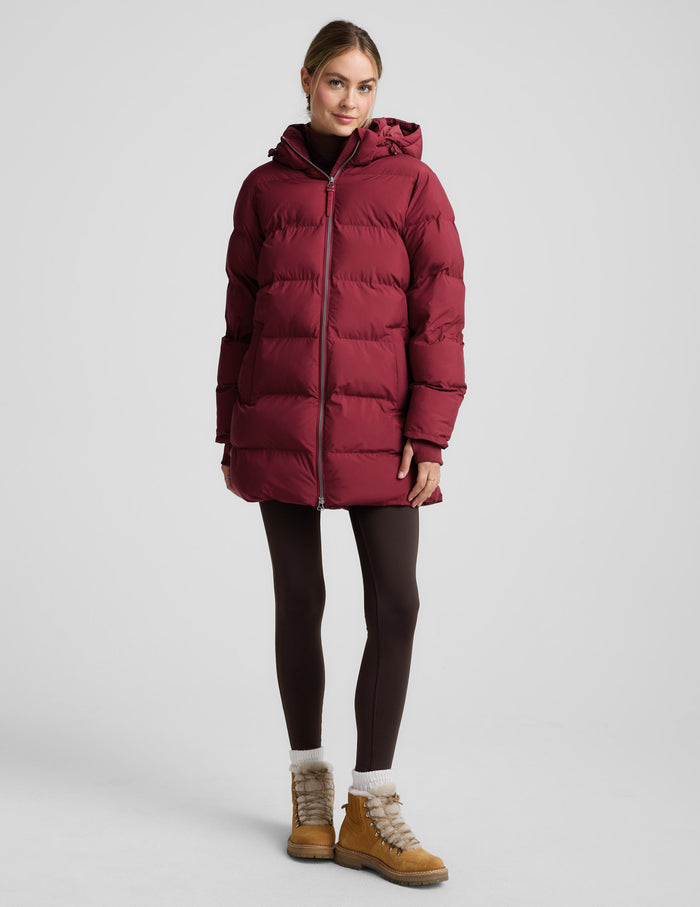 Woman wearing a red puffer coat on a light gray background.