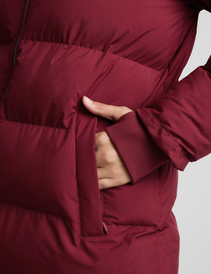 Woman wearing a red puffer coat on a light gray background.