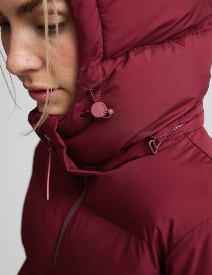 Woman wearing a red puffer coat on a light gray background.