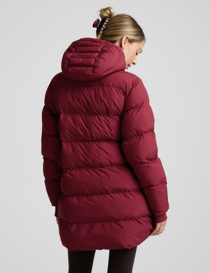 Woman wearing a red puffer coat on a light gray background.