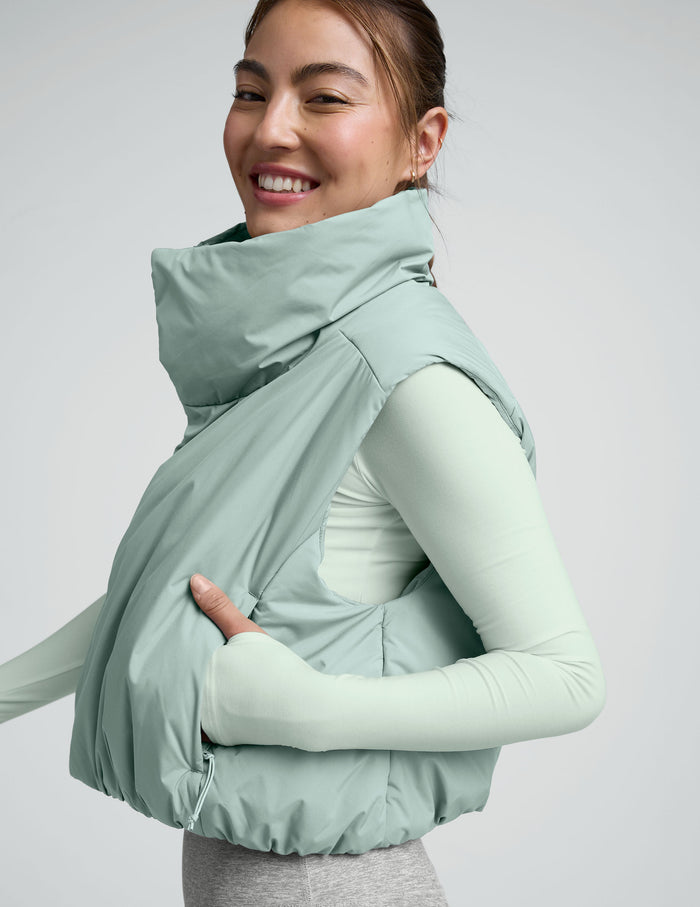 Woman wearing a light blue cropped puffer vest on a plain background.