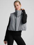 model wearing a gray puffer vest over a black long sleeve and leggings on a light gray background.