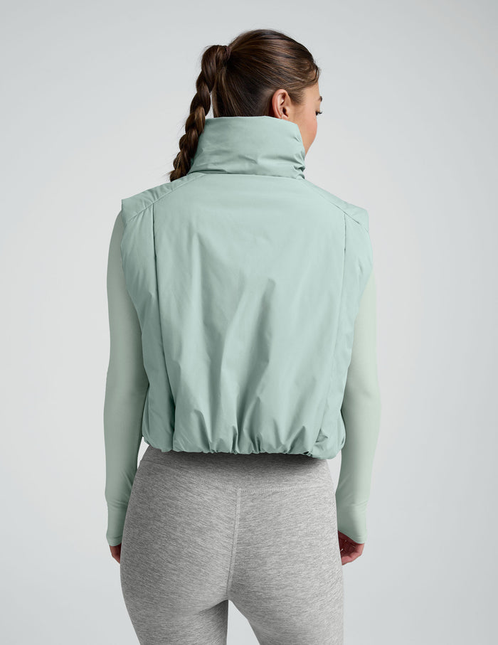 Woman wearing a light blue cropped puffer vest on a plain background.