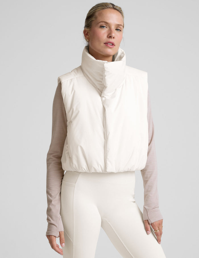 model wearing a white puffer vest over a long-sleeve shirt on a light gray background.