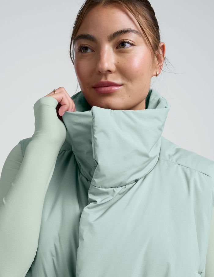 Woman wearing a light blue cropped puffer vest on a plain background.