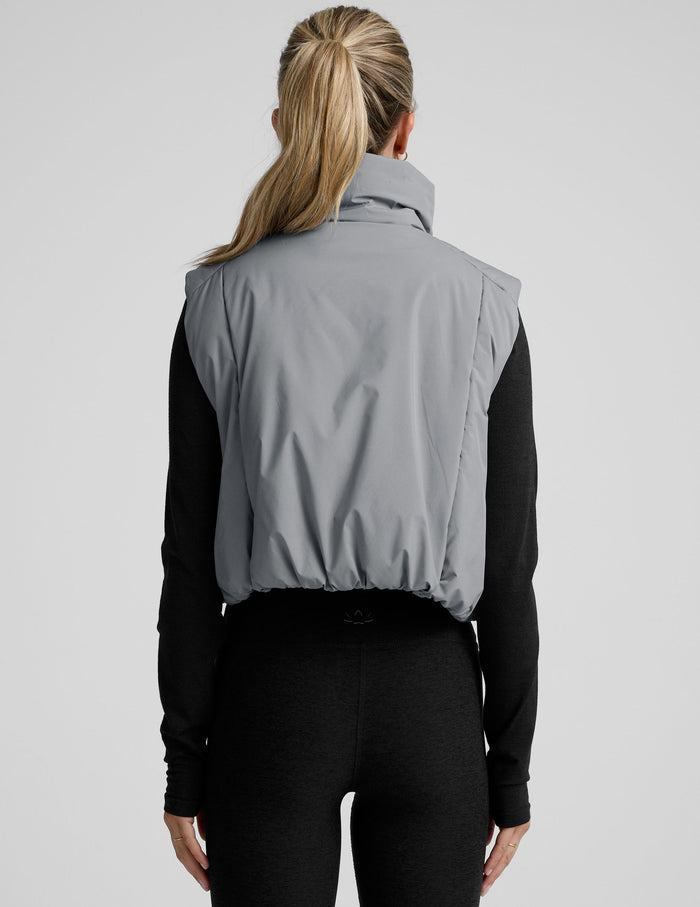 model wearing a gray puffer vest over a black long sleeve and leggings on a light gray background.