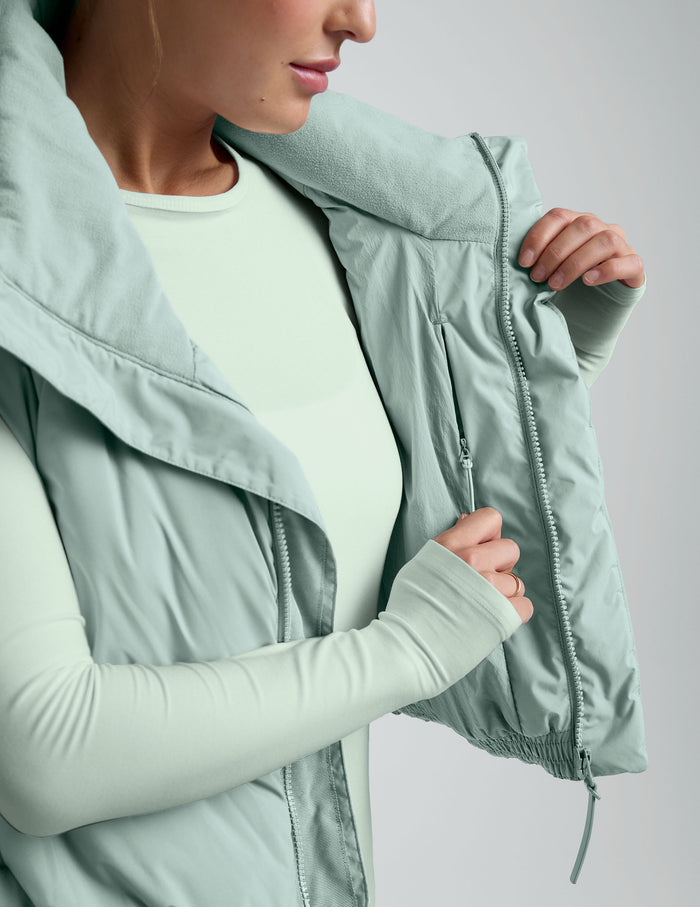 Woman wearing a light blue cropped puffer vest on a plain background.