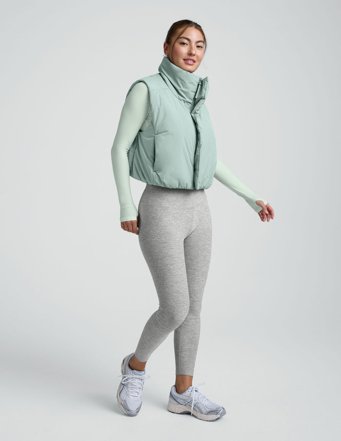Woman wearing a light blue cropped puffer vest on a plain background.