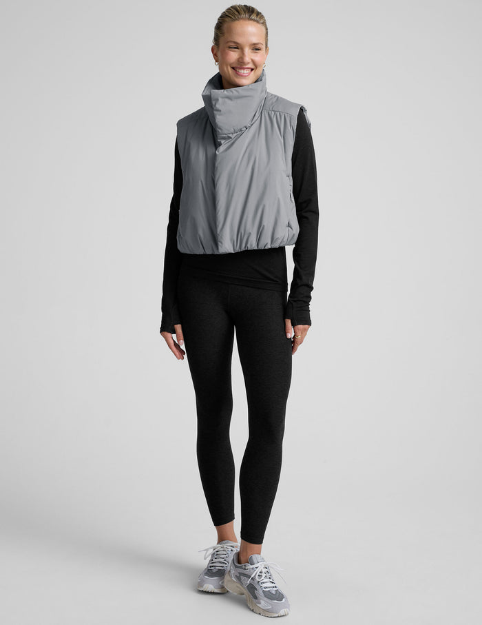 model wearing a gray puffer vest over a black long sleeve and leggings on a light gray background.