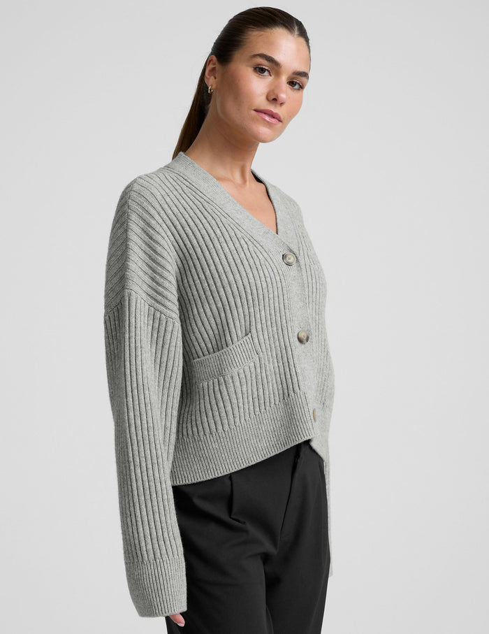 woman wearing a gray ribbed cardigan on a plain background.