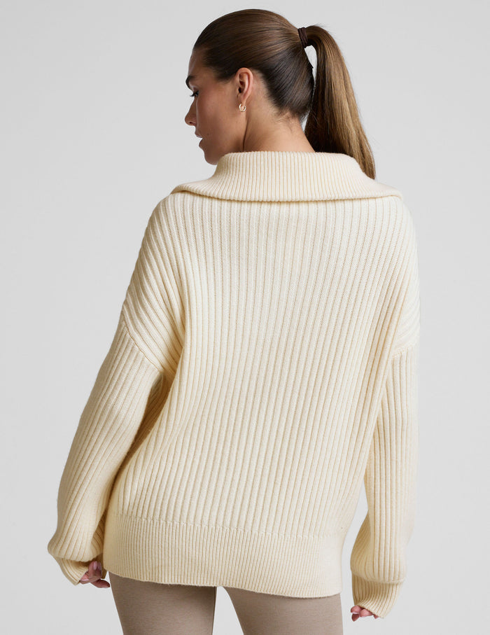 woman wearing a white quarter zip collared sweater against a plain background.
