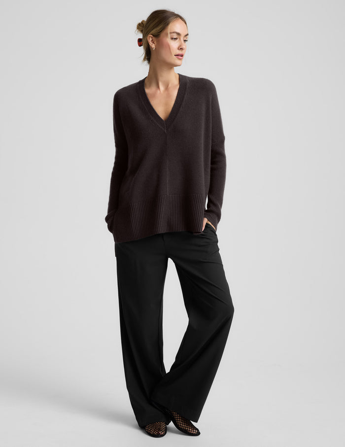 Woman wearing a brown v-neck long length sweater against a plain background.