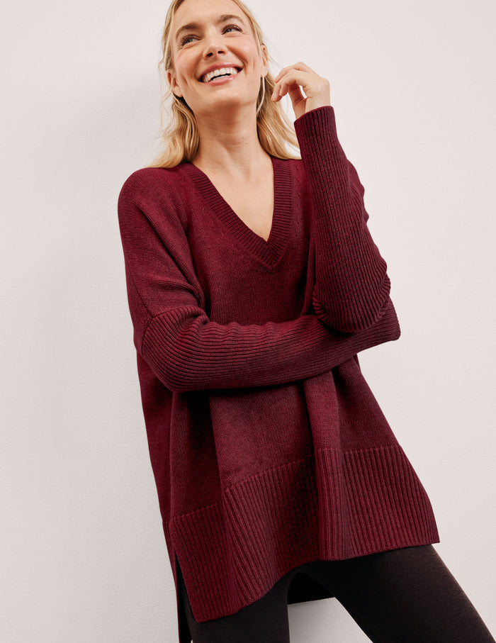 woman wearing a red v-neck sweater sweater against a plain background.