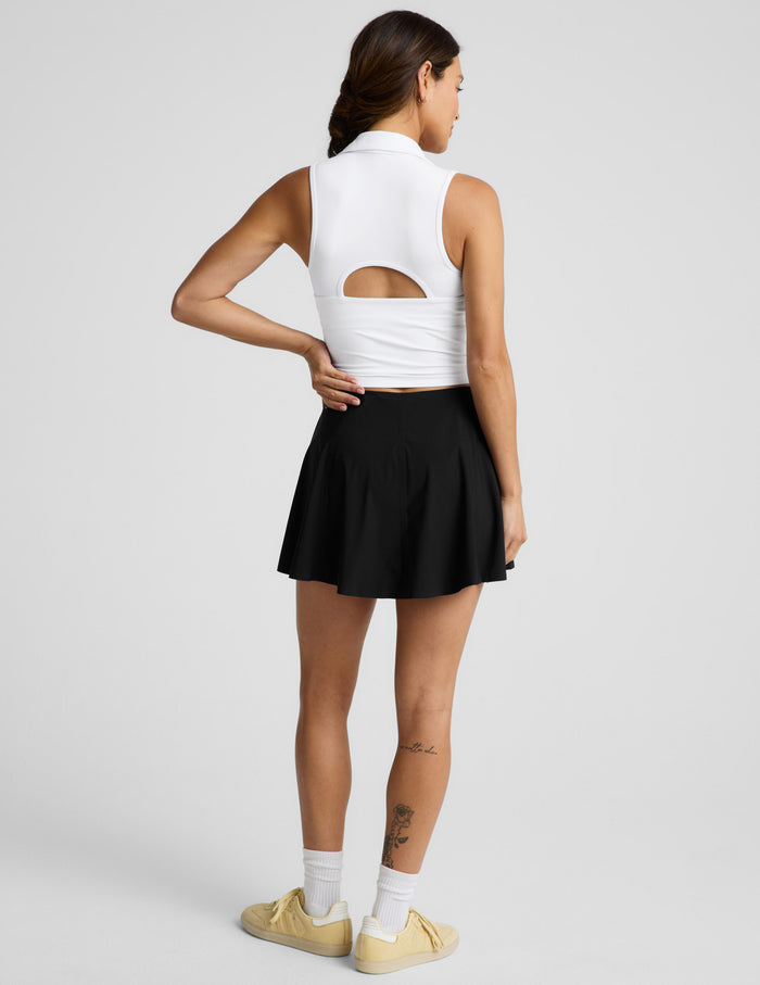 Woman wearing the Black You're A force Skirt™ with a white sleeveless top and yellow sneakers, shown from a rear view.